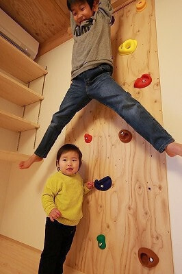 ロフト下。ボルダリングウォールを背に雲梯にぶら下がるお子さんと、その下に立つお子さん。